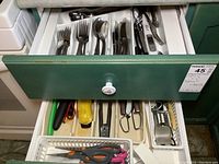 Top green drawer open showing organized Reed and Barton stainless steel forks, spoons, knives and kitchen scissors in plastic tray; additional utensils and tools below with plastic peelers and metal utensils visible.