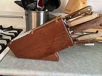 Side view of wooden block holding multiple knives and tools showing wooden handles and metal rivets.