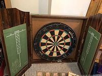 Open wooden dart board cabinet showing the dart board and chalkboard score counters on both doors.