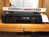 Front view showing Philips DVD player silver unit on top of black Sony 5 disc CD changer unit on wood cabinet shelf.