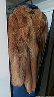 Brown fur coat hanging, showing side and front fur texture.