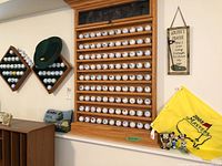 Wide angle of golf memorabilia collection showing large rectangular and two diamond-shaped golf ball display racks with balls from different courses, yellow 2008 Masters flag and wall decor