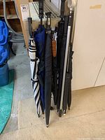 Side view showing eight golf umbrellas in different dark colors with various handles and a ball retriever with silver metal shaft.