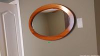 Front view of an oval wall mirror with a medium tone wooden frame hanging on a wall.