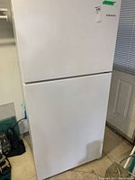 Front view of white Amana refrigerator with two doors, top freezer and bottom fridge compartment, showing brand label.
