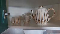 Sadler brand tea pot, creamer and sugar bowl with cream color and gold vertical stripes, displayed inside a cabinet.