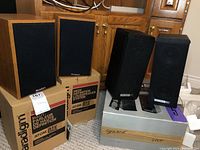 Pair of Paradigm Atom speakers shown on top of their original packaging boxes labeled "Atom Oak High Definition Loudspeaker System" in oak wood finish with black fabric covers.