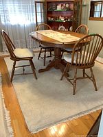 Dining table and four Windsor style chairs arranged around it on a light area rug, with a decorative table runner on the table.