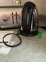 KitchenAid 4-slice stainless steel toaster next to stainless steel and black electric kettle on countertop with power cords visible.