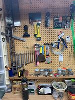 Wide view of assorted hand tools and hardware items hanging on pegboard including saws, wrenches, paint scrapers, and jars of hardware.