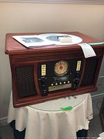 Front and side view of wooden music center showing analog dial and control buttons with speaker grills