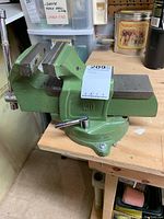 Green swivel bench vise on wood workbench, showing the jaws and rotating base.