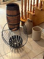 Wooden barrel, black wire baskets, ceramic jug and crock shown together on tile floor near stairs.