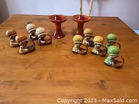 Photo showing the full set of five bonneted girl ceramic napkin rings with baskets and two red pedestal candle holders on a wooden table.