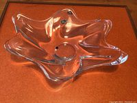 Top view showing overall form of clear glass bowl with flowing organic edges on orange background.