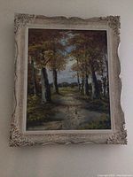 Framed painting showing overall view of tree-lined path with ornate cream-colored frame having some wear and chips.