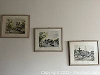 Three framed art prints hanging on a wall showing scratches on frames and scenes including urban and natural environments
