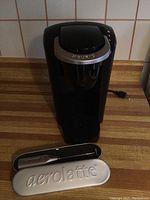 Keurig coffee maker front view with Aerolatte frother case in foreground