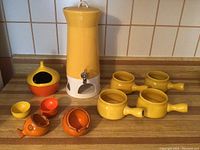 Full set including tall yellow beverage dispenser, four yellow handled soup bowls, two orange fish-shaped bowls, and several small yellow and orange bowls arranged on countertop.