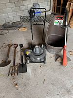Full view of all garden tools and equipment including manual push lawn mower, string trimmer, garden container, and four hand tools.