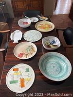 Overview of nine decorative platters and dishes arranged on a wooden table, showing various sizes, shapes, and colorful designs.