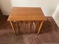 Rectangular wooden table viewed from top showing surface wear and chips, with stools nested underneath