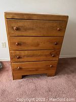 Front view of wooden chest showing four drawers with round wooden knobs, surface with some scratches and dust.