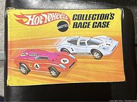 Front side of the yellow and orange Hot Wheels Collector's Race Case showing graphics of two race cars and Mattel logo.