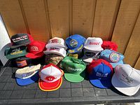 Overview photo showing all 21 vintage fishing ballcaps arranged on a table outside against wood background.