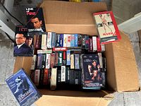 Full box view showing the mix of Betamax and VHS tapes inside a cardboard box, titles and covers visible