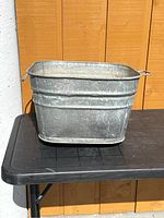 Front view of the antique metal wash tub showing its rectangular shape, patina, and side handles.