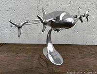 Front angled view of chrome airplane collectible on curved stand showing four propellers.