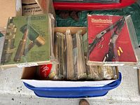 Large box filled with multiple sealed vintage hunting and sports magazines, showing colorful covers with images of rifle cartridges and firearms.