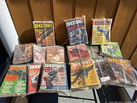 Photo showing 14 Sporting Magazines from 1970s to 1980s, mostly Shooting Times issues with some in plastic sleeves.