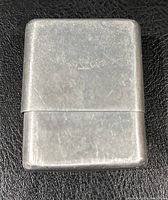 Aluminum cigarette pack holder with visible wear on a black surface.