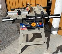 Front view of RYOBI 10-inch table saw on metal stand with control panel and adjustable fence system visible.