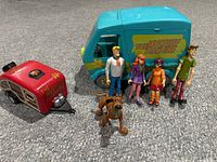 Front view of all five Scooby Doo action figures arranged in front of the blue Mystery Machine van and separate red trailer with branding visible.