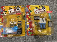 Two Simpsons action figures still in blister packs on original cards. Shows overall condition and packaging detail.
