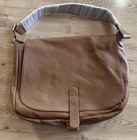 Front view of the tan leather messenger bag showing leather flap with buckle strap and padded adjustable shoulder strap.