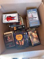 Box containing assorted VHS movies showing titles The Graduate, Blood Simple, A Good Stitch in Time, Doctor Zhivago, others visible