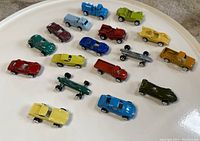 Photo of 17 vintage 1980s Tootsie mini diecast cars arranged on a white tray, showing various models in multiple colors from different angles.