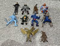 Photo of lot showing 10 vintage plastic action figures from various 1980s/90s toy lines including MOTU, TMNT, and Godzilla. Figures laid out on carpet.