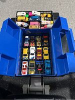 Blue plastic Matchbox carry case open showing 24 diecast cars arranged in trays with some cars visible brightly colored including yellow, red, white, blue cars