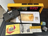 Opened original box showing Kodak Instamatic S-20 camera inside with strap, flash cube, instruction manual and film cartridge.