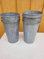 Front view showing two stacks of tall vintage metal maple sap tins against a wooden background.