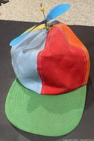 Front and side view showing multicolored panels with a green brim and a blue propeller attached on top with a yellow ball tip.