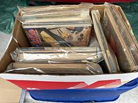 Top view of a cardboard box with multiple vintage sport magazines mostly sealed in plastic, some wear visible on covers.