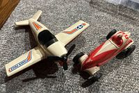 Fisher-Price white airplane and 1970s Sunruco red and white race car on carpeted floor.