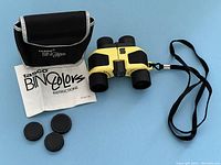 Overview of binoculars, case, instruction manual, lens caps, and strap on a blue background