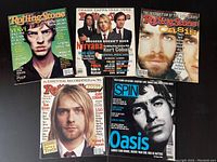 Five magazines arranged on a flat surface, showing covers of Rolling Stone and Spin magazines from the 1990s with notable musicians like Mick Jagger, Kurt Cobain, and Oasis.